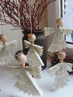 some paper angel ornaments hanging from strings on a window sill with pine cones and branches in the background