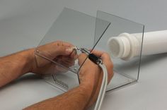 a man is cutting glass with scissors on a white table and gray wall behind him