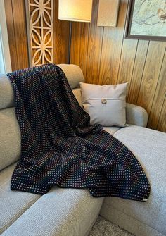 a couch with a blanket on top of it next to a lamp and pillows in front of a wood paneled wall