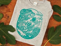 a t - shirt with an image of a mermaid on it and leaves surrounding it