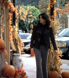 a woman walking down a sidewalk next to pumpkins