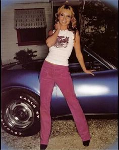 a woman standing next to a car with her hand on her hip and posing for the camera