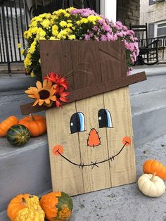 a wooden sign with a scarecrow face on it and pumpkins in the foreground