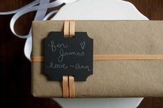 a gift wrapped in brown paper with a chalkboard tag attached to it and writing on the side