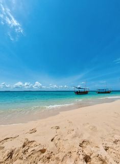 two boats sitting on top of a sandy beach next to the ocean with clear blue skies