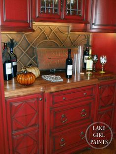 a kitchen with red cabinets and wine bottles on the counter top in front of it