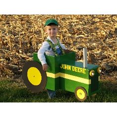 a young boy sitting in a toy tractor on top of green grass and yellow leaves