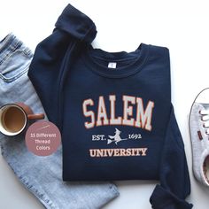 Salem University Halloween Sweatshirt Celebrate Halloween in collegiate style with our Salem University Halloween Sweatshirt! This unique sweatshirt combines the charm of Halloween with the classic varsity look, making it perfect for any Halloween enthusiast. Key Features: - Design: Embroidered 'Salem' in college varsity font on the front chest, followed by 'EST. Year' and a witch, with 'University' at the bottom in varsity font. - Customization: Choose two thread colors: one for the outline of Collegiate Team-colored Sweatshirt For Fall, College Team-colored Sweatshirt For Fall, Varsity T-shirt With Embroidered Graphics For Fall, Crew Neck T-shirt With University Logo For Fall, School Spirit Sweatshirt With Team Name For Fall, College Team Name Sweatshirt For Fall, Varsity T-shirt For College In Fall, College Team Spirit T-shirt For Fall, College Fall Fan Apparel T-shirt