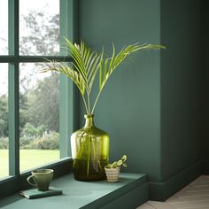 a green vase sitting on top of a window sill next to a cup and plant