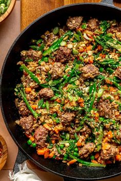 a skillet filled with meat and vegetables on top of a wooden table