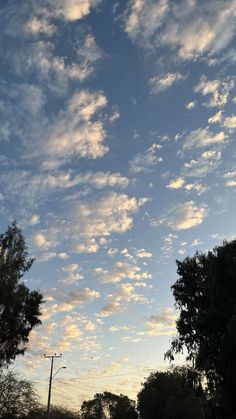 the sky is filled with clouds and some trees in front of an empty street at dusk