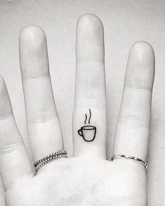 a person's hand with a coffee cup tattoo on their left thumb and the middle finger