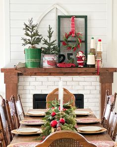 a dining room table set for christmas with plates and place settings on it, along with greenery