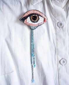 a close up of a person wearing an eye brooch with beads and chains hanging from it