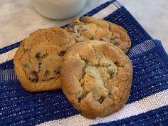 three chocolate chip cookies on a blue and white towel next to a glass of milk