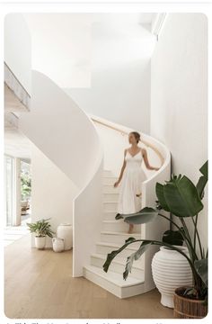 a woman in a white dress is standing at the top of a spiral stair case