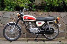 a red and white motorcycle parked next to a stone wall