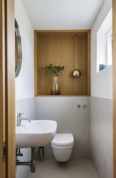 a white toilet sitting next to a bathroom sink in a bathroom under a window with wooden trim