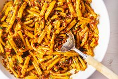 a white bowl filled with pasta covered in sauce and topped with a wooden serving spoon