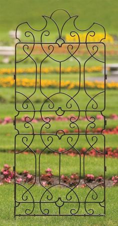 an iron garden trellis in the middle of a field with flowers and grass behind it