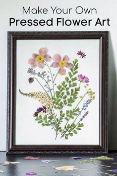 pressed flower art is displayed in a frame on a table with flowers and leaves around it