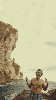 a man standing on top of a rocky beach next to the ocean with his hands in the air