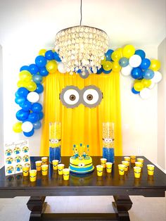 a table with yellow and blue decorations on it, including a monster face balloon over the top