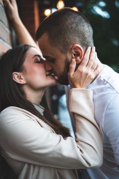 a man and woman kissing in front of a brick wall