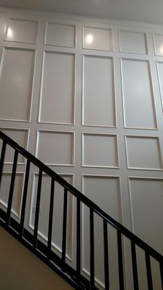 a stair case next to a wall with white paneling and black handrails