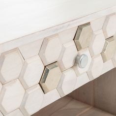 a white marble table with hexagonal tiles on the top and drawer knobs