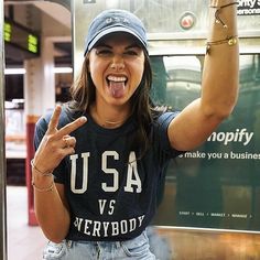 a woman making a funny face while standing in front of a sign that says usa v's everybody