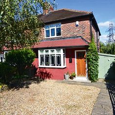 a red brick house sitting next to a lush green tree and shrubbery in front of it