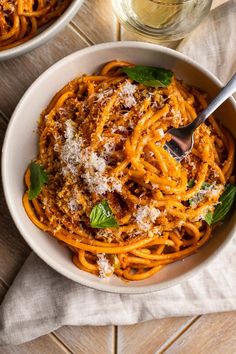 two bowls filled with spaghetti and topped with parmesan cheese, basil leaves and parmesan