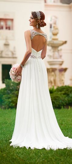 a woman in a wedding dress standing on the grass with her back to the camera