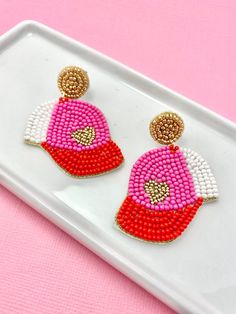 two pink and white beaded earrings on a tray with a pink surface in the background