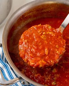 a ladle full of marinara sauce being stirred with a spoon