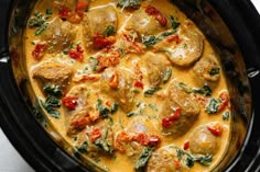 a close up of food in a crock pot with spinach and tomatoes on top