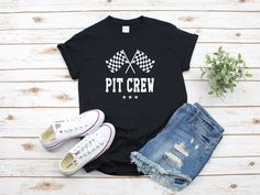 a t - shirt that says pit crew with two crossed flags on it and ripped jeans