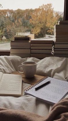 a cup of coffee, notebook and pen on a bed in front of a window