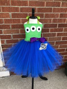 a green and blue dress with googly eyes is on display in front of a brick wall