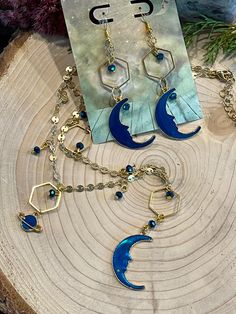 Blue moon, Saturn, and star charms on a gold disc chain with hexagonal gold wire accents and glass bead dangles Celestial Metal Jewelry With Dangling Charms, Brass Dangle Jewelry With Star Charm, Moon And Star Necklace, Bead Dangles, Sun Designs, Gold Disc, Moon And Star, Moon Earrings, Gold Wire