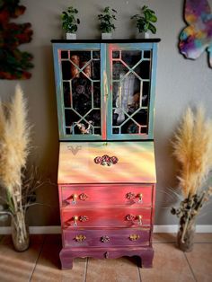 an old dresser painted pink, yellow and green with decorative glass inserts on the doors