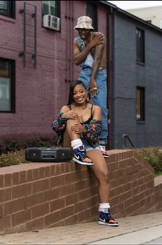 a woman sitting on the side of a brick wall next to a man with his arms around her