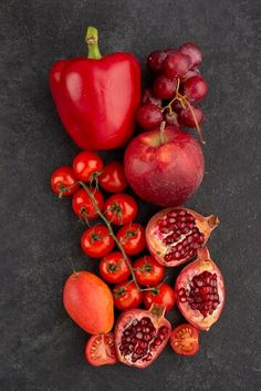 pomegranates, tomatoes, and other fruits are arranged on a black surface