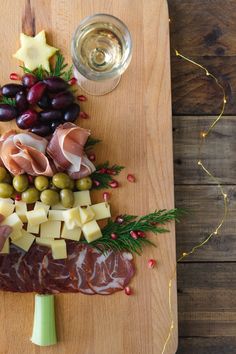 a wooden cutting board topped with meat, cheese and olives next to a glass of wine