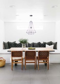 a dining room table with four chairs and a bench in front of it, surrounded by pillows