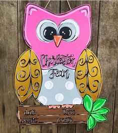 a pink and yellow owl sitting on top of a wooden sign