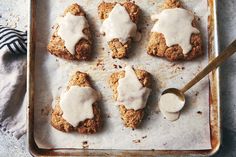 six biscuits covered in white icing on a baking sheet with a spoon next to them