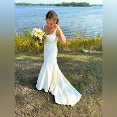 a woman in a white wedding dress standing by the water holding a bridal bouquet