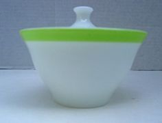 a white and green bowl sitting on top of a table next to a wall with a gray background